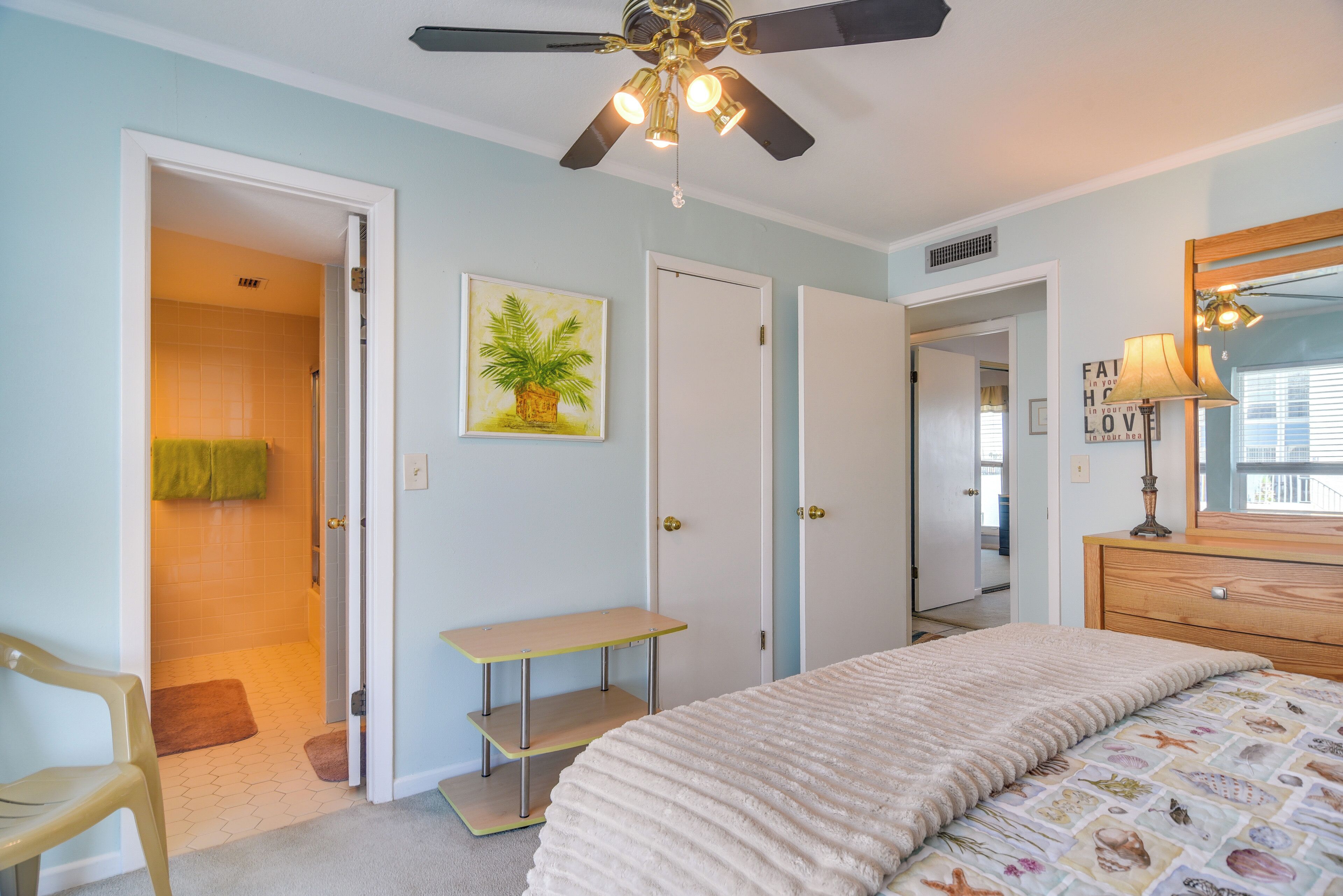 A bedroom with a bed, a ceiling fan, a desk, and a door leading to a bathroom.
