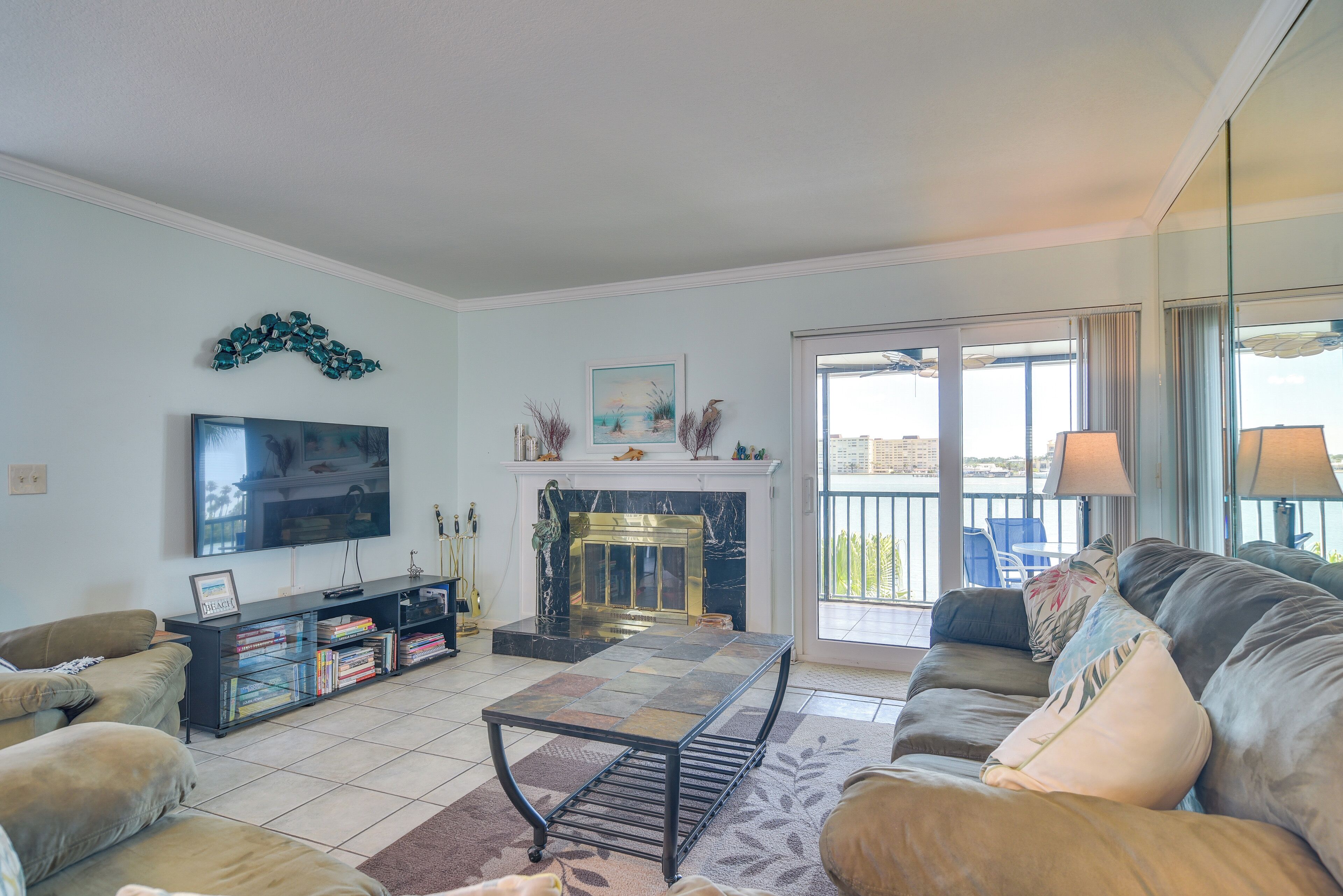 A living room with a fireplace, a television, a sofa, and a balcony with outdoor furniture.
