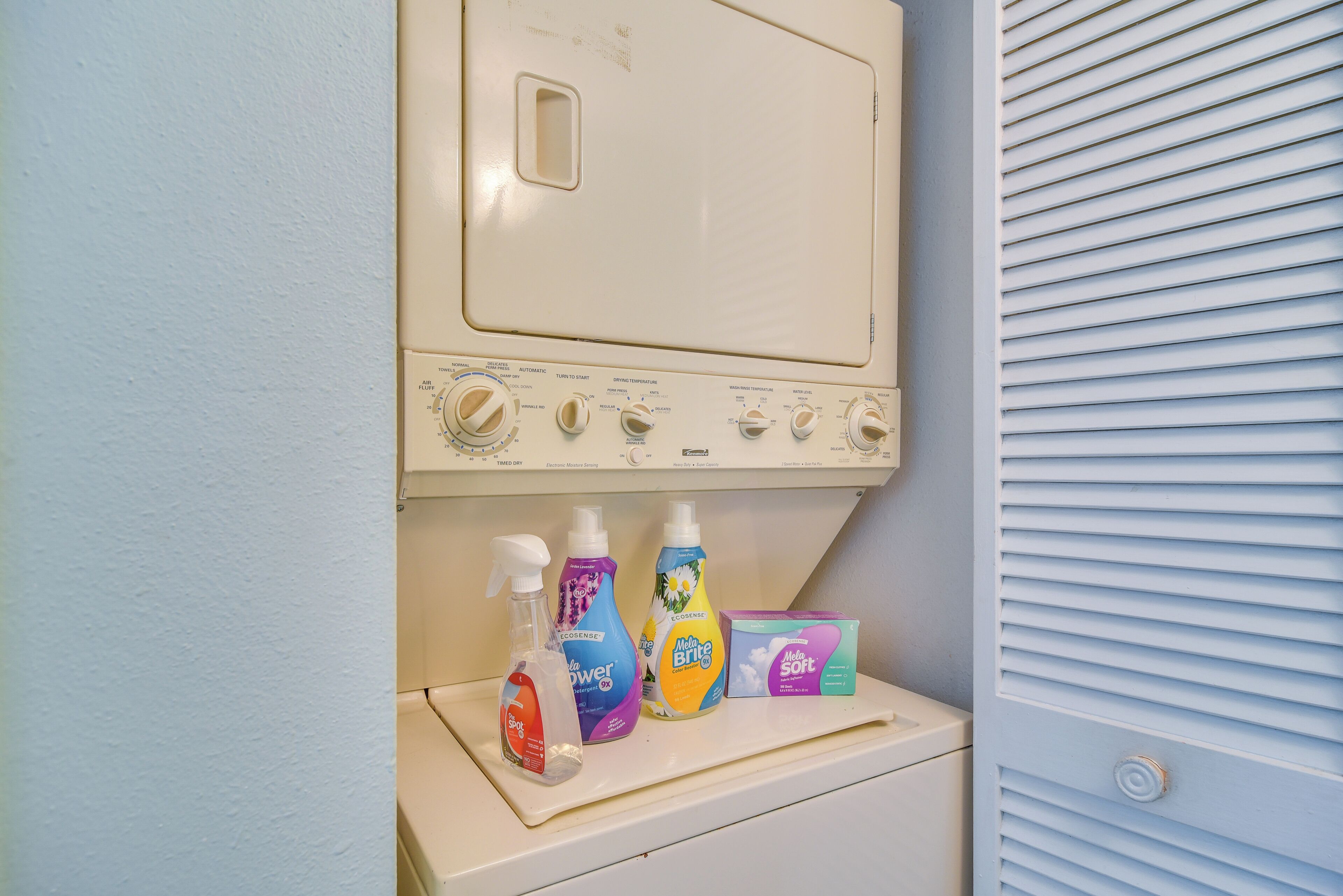 A front-loading washing machine with detergent bottles and a box.