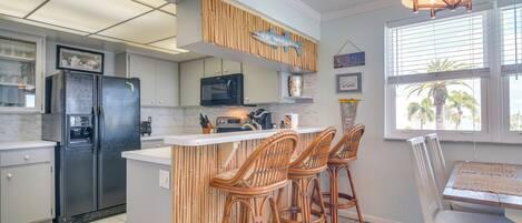 Una cocina con un refrigerador negro, armarios blancos, un microondas y una isla de madera con taburetes de bar.