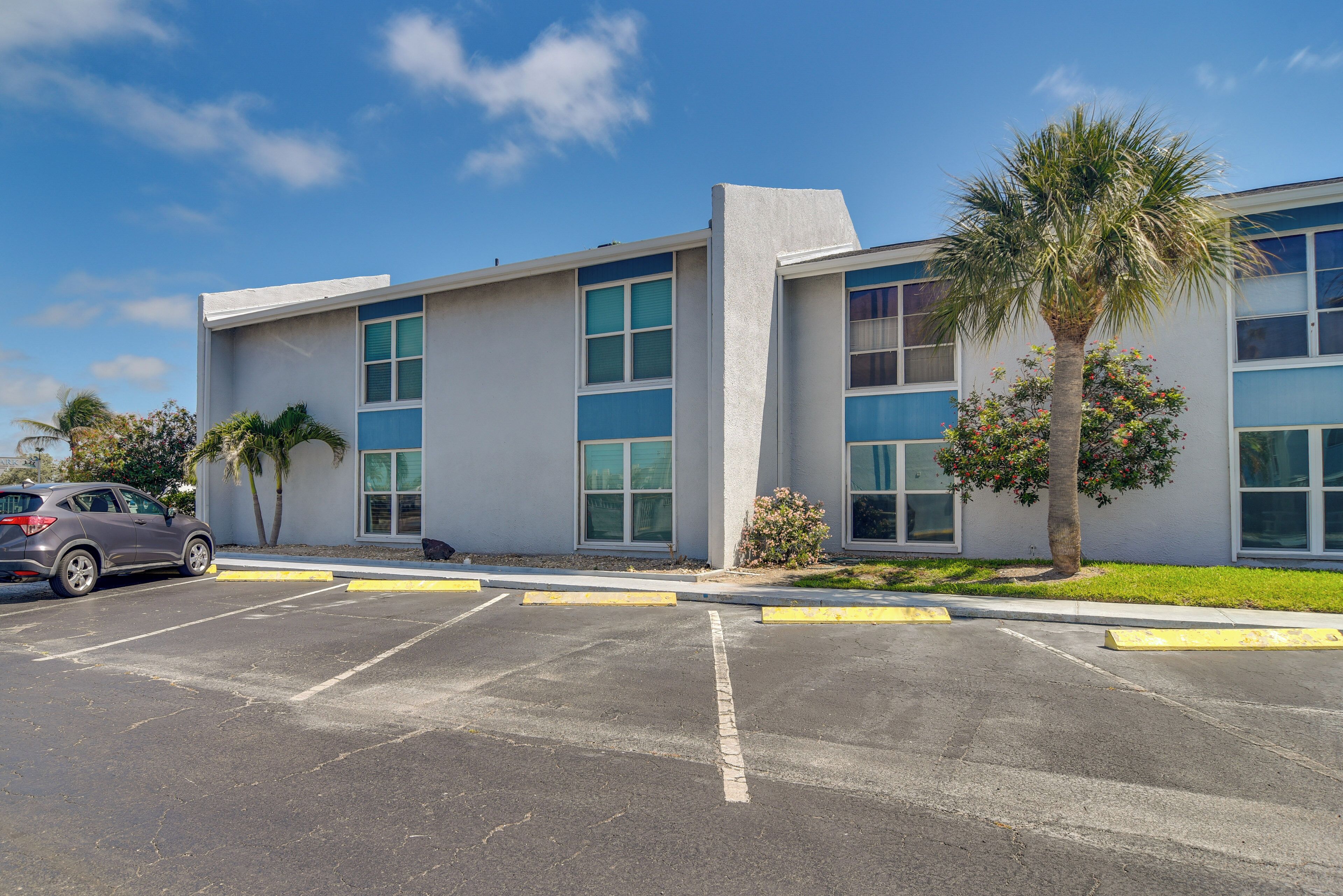 A modern building with a parking lot, a car, and a palm tree.