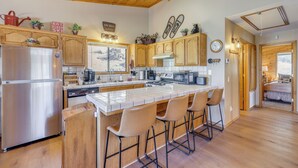 A kitchen with wooden cabinets, a stainless steel refrigerator, a large island with bar stools, and a view of a mountainous landscape. - Alpine Luxury & Mtn Views: Family Big Bear Escape! (Big Bear Lake)