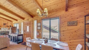 A wooden cabin interior with a dining table, chairs, a fireplace, and a sign that reads 'Adventure Awaits.' - Alpine Luxury & Mtn Views: Family Big Bear Escape! (Big Bear Lake)