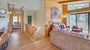 A wooden interior with a sofa, a dining area, and a view through large windows. - Alpine Luxury & Mtn Views: Family Big Bear Escape! (Big Bear Lake)