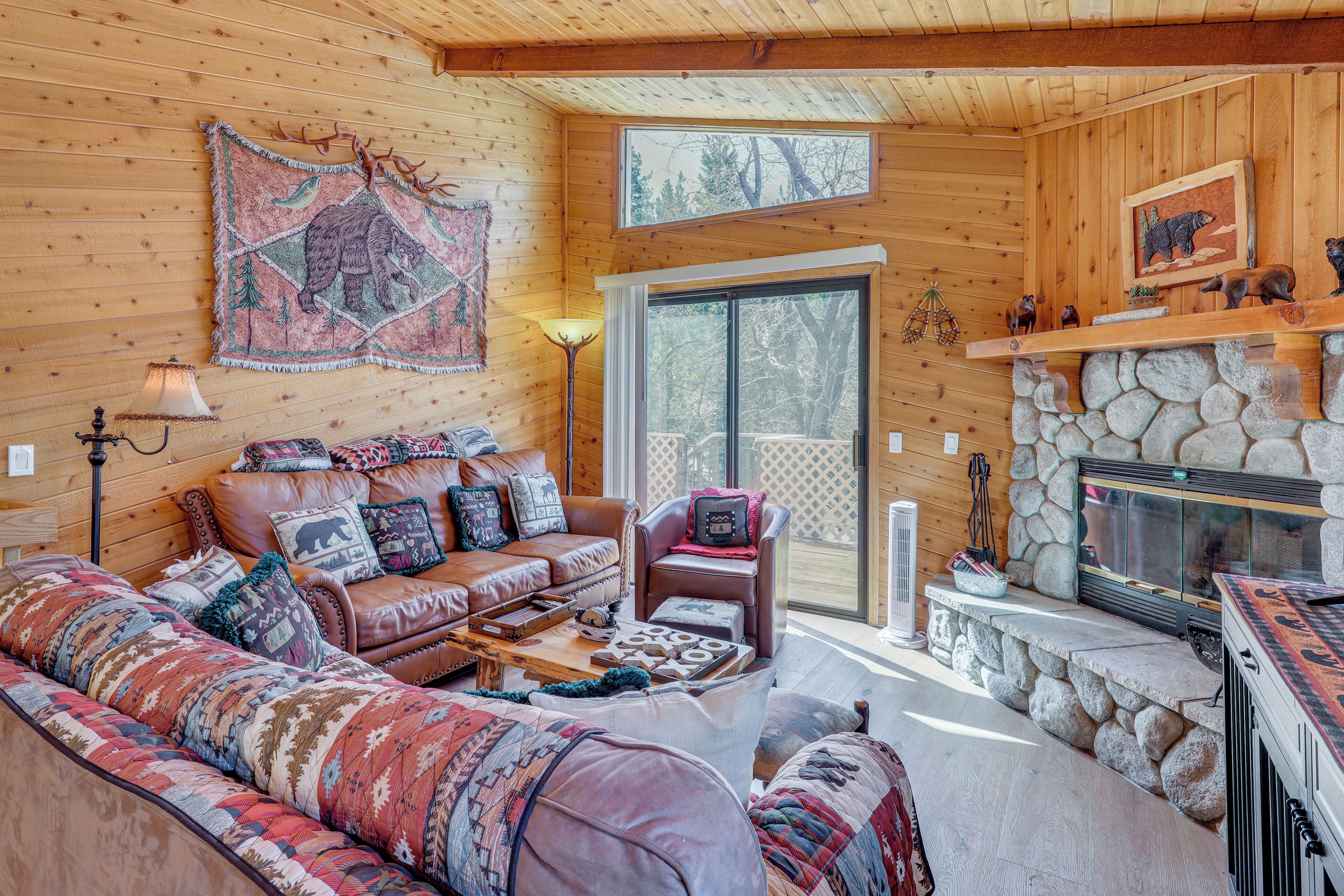 A log cabin interior with a leather sofa, a stone fireplace, and a large window.