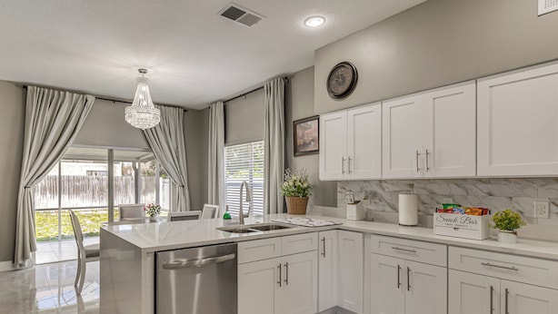 A kitchen with white cabinets, a stainless steel dishwasher, a marble backsplash, and a chandelier. - Screened Lanai & Yard! Family Getaway in Apopka (Apopka)