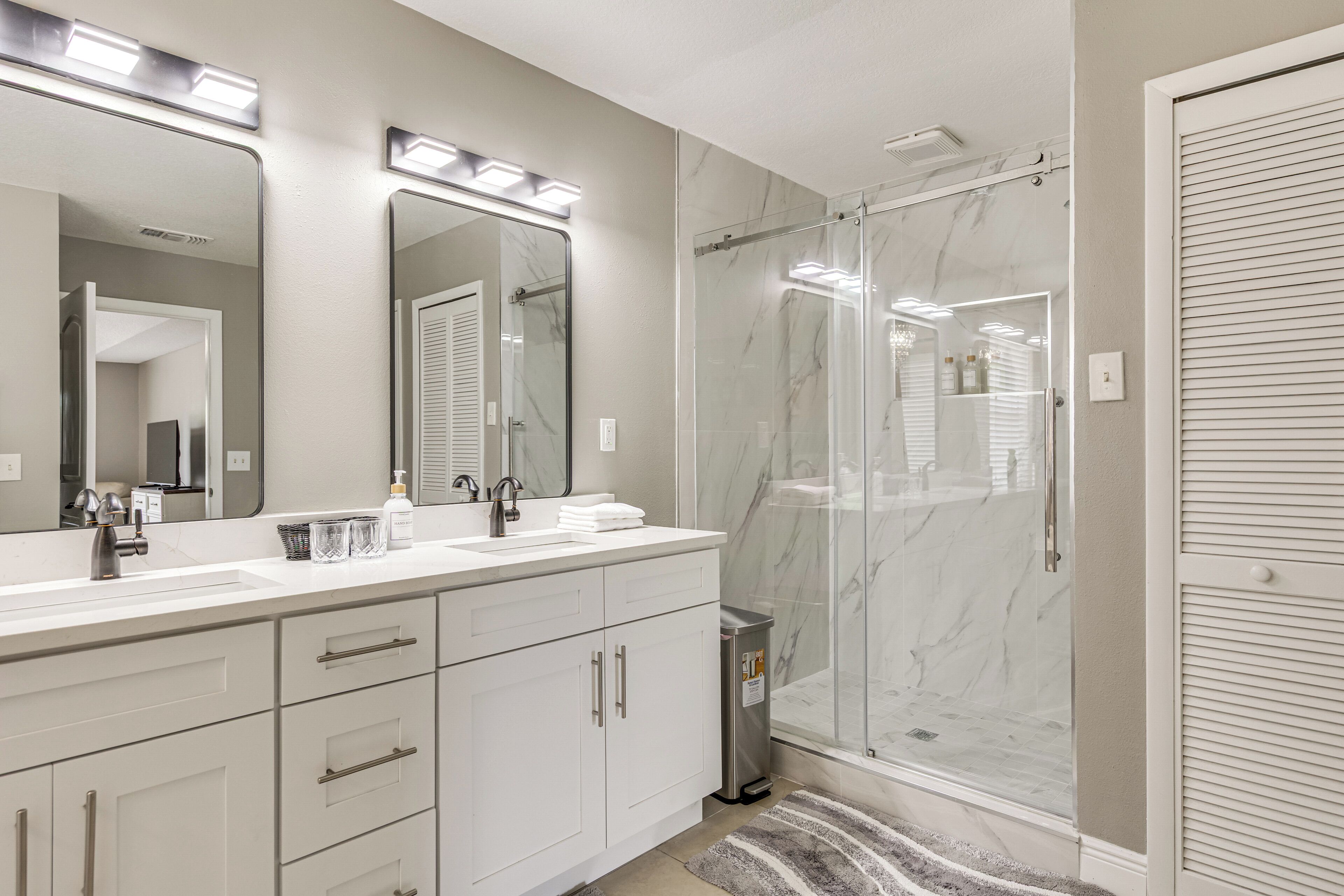 Une salle de bain moderne dotée d’un grand miroir, de deux vasques, d’une cabine de douche et d’un dressing.