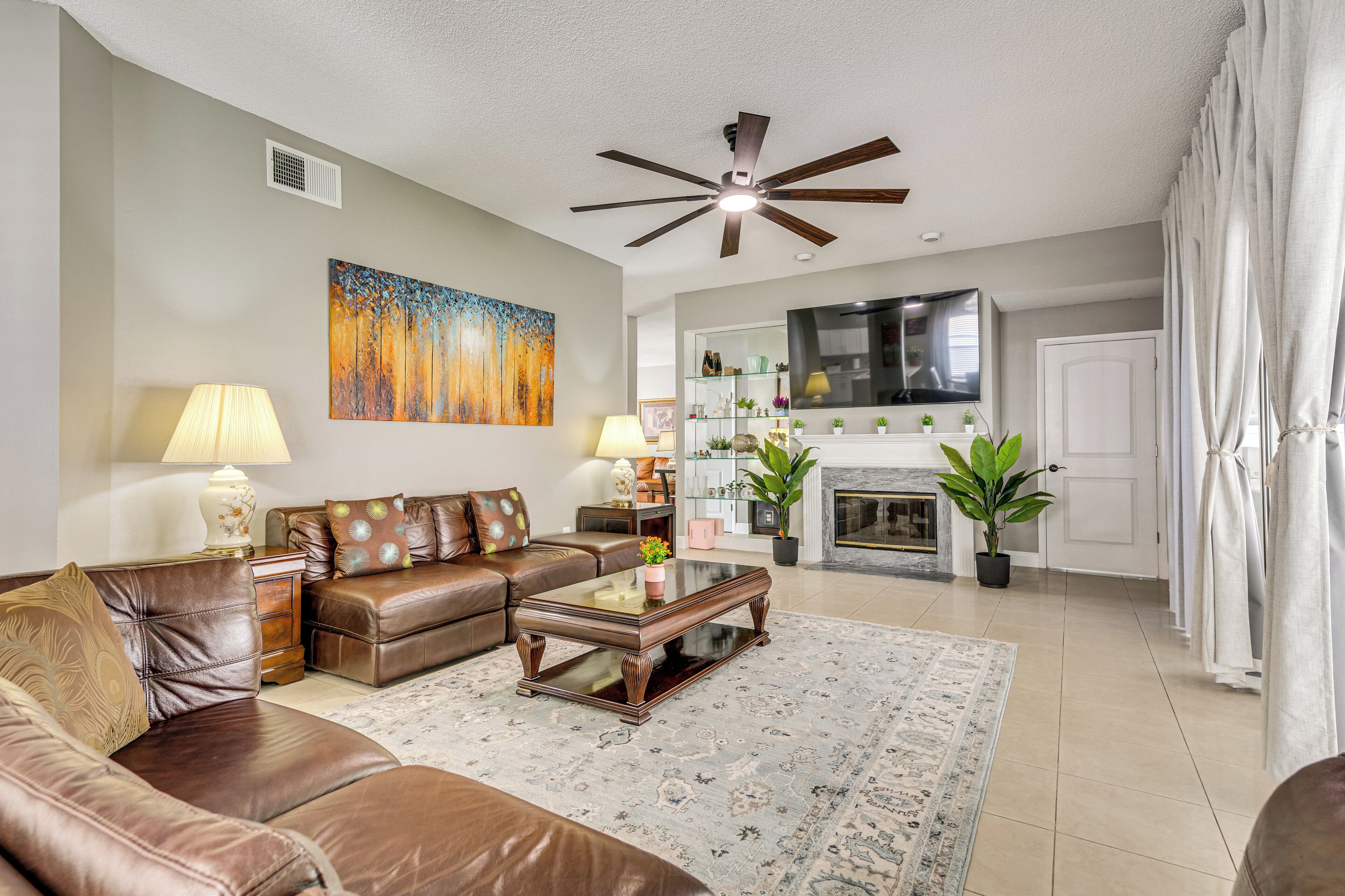 A living room with a brown leather sofa, a glass coffee table, a fireplace, and a ceiling fan.