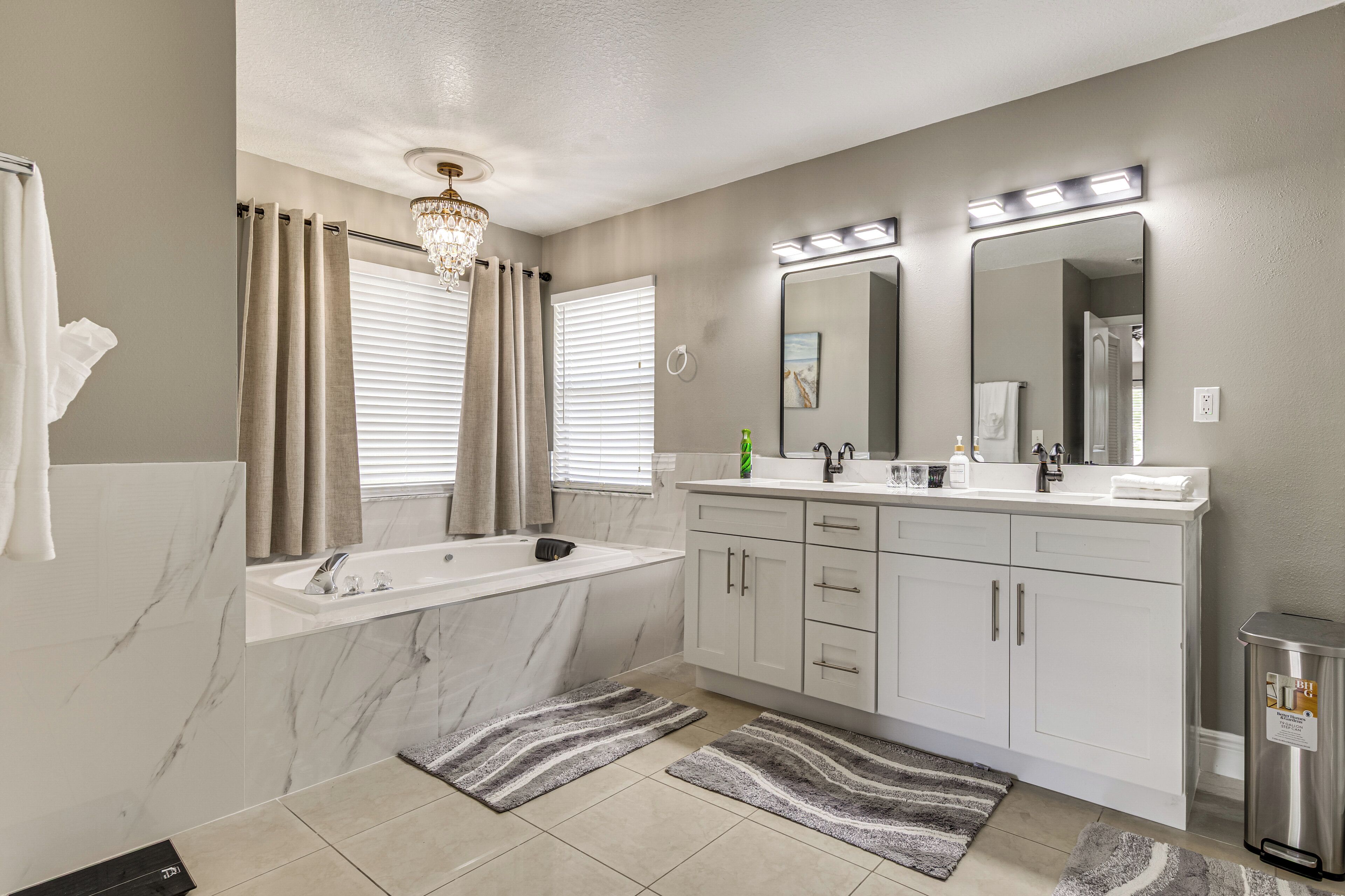 A bathroom with a marble sink, a bathtub, a vanity with a mirror, and a chandelier.