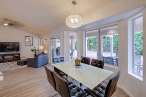 A spacious living room with a large glass table, leather chairs, a sofa, a television, and a chandelier. - Golf, Swim, Play & Relax! Gated Sun Lakes Home (Chandler)