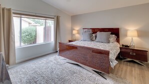 A bedroom with a large bed, two bedside tables with lamps, a window with curtains, and a carpeted floor. - Golf, Swim, Play & Relax! Gated Sun Lakes Home (Chandler)