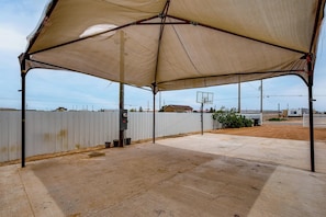 An outdoor covered area with a basketball hoop, concrete flooring, and a white fence in the background. - Family Friendly! Rural El Paso Home: Patio & Grill (El Paso)