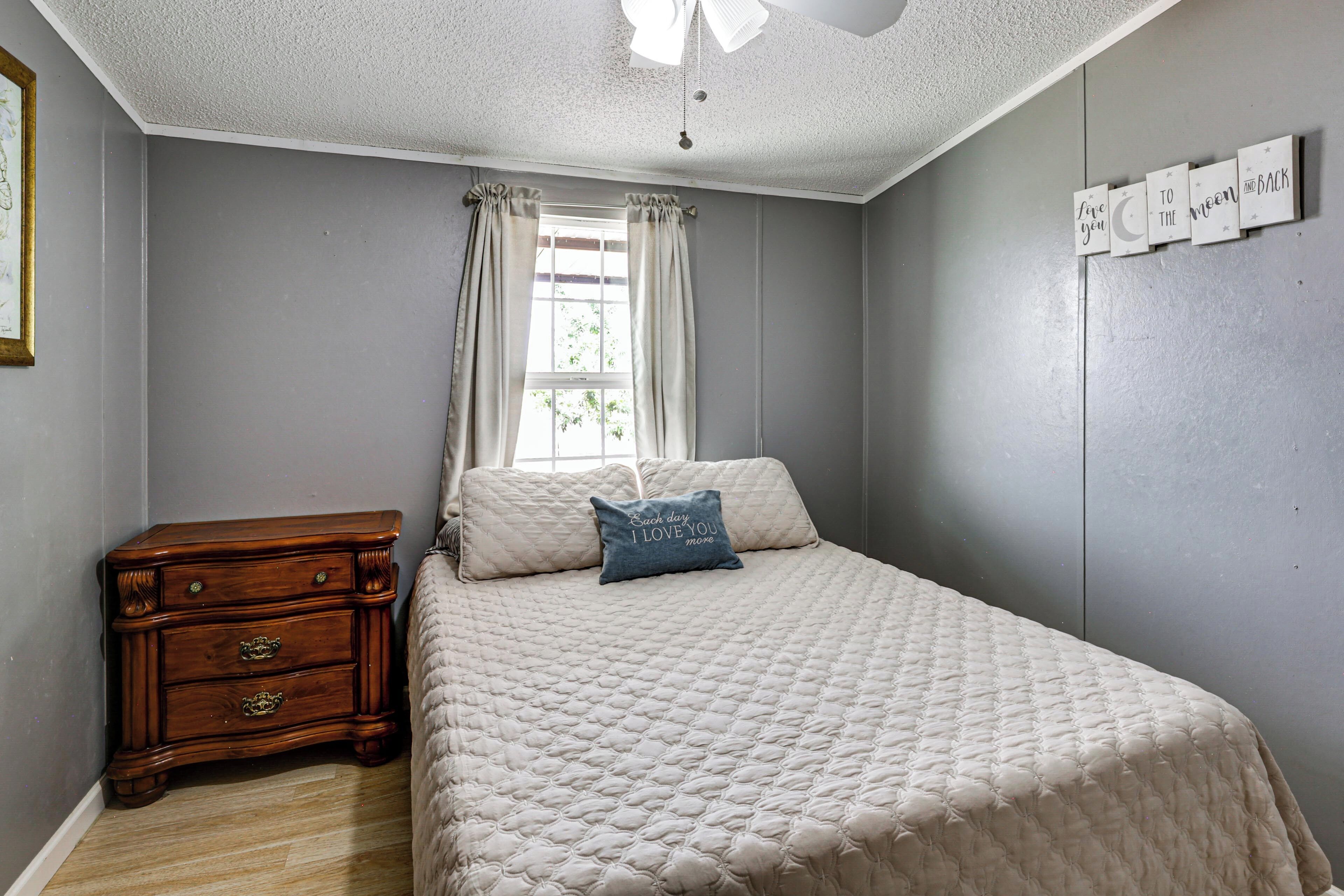 A bedroom with a bed, a nightstand, a window with curtains, and a wall with a sign.