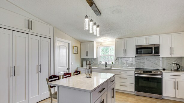A modern kitchen with white cabinetry, a central island, stainless steel appliances, and pendant lighting.