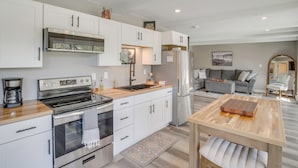 A modern kitchen with white cabinetry, stainless steel appliances, a wooden countertop, and a dining area with a wooden table and bench. - The Cottage on Lake Bernice - Campbellsport (Campbellsport)