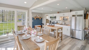 A spacious kitchen with white cabinetry, a dining area with a wooden table, and a large window offering a view of the outdoors. - The Cottage on Lake Bernice - Campbellsport (Campbellsport)