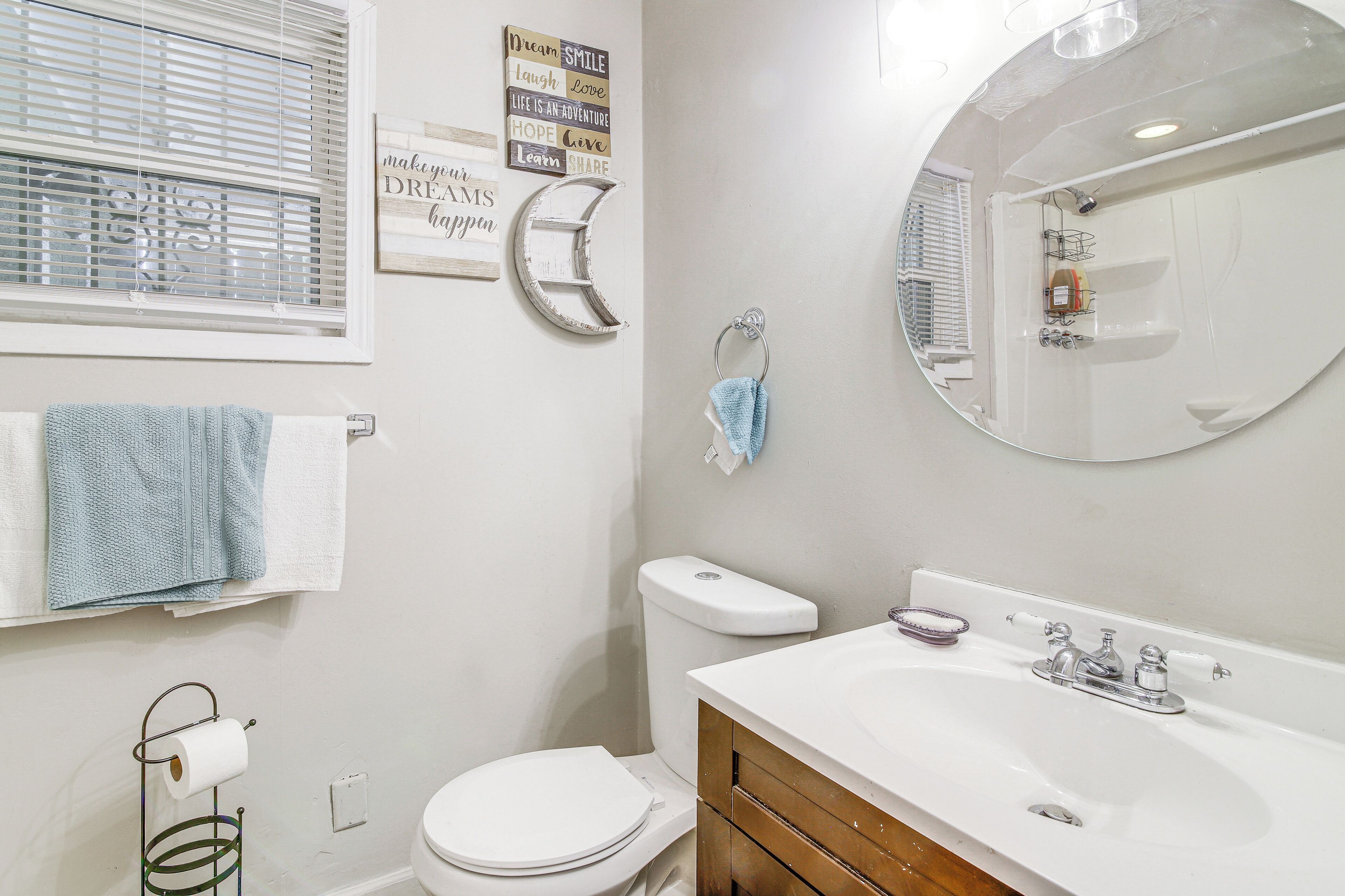 A bathroom with a toilet, sink, mirror, towel rack, and motivational wall art.