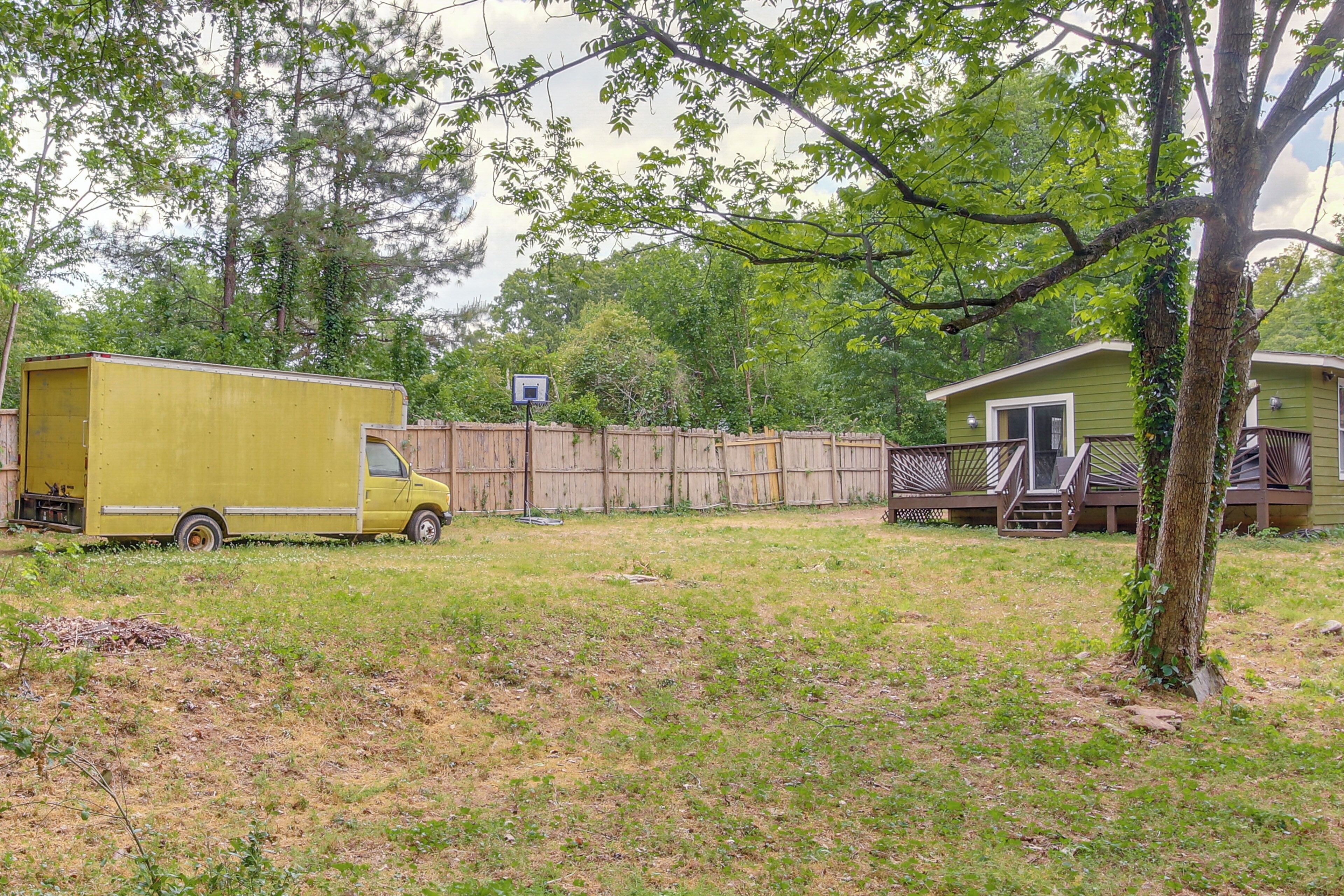 A green mobile home with a deck, a fenced yard, and a yellow truck.