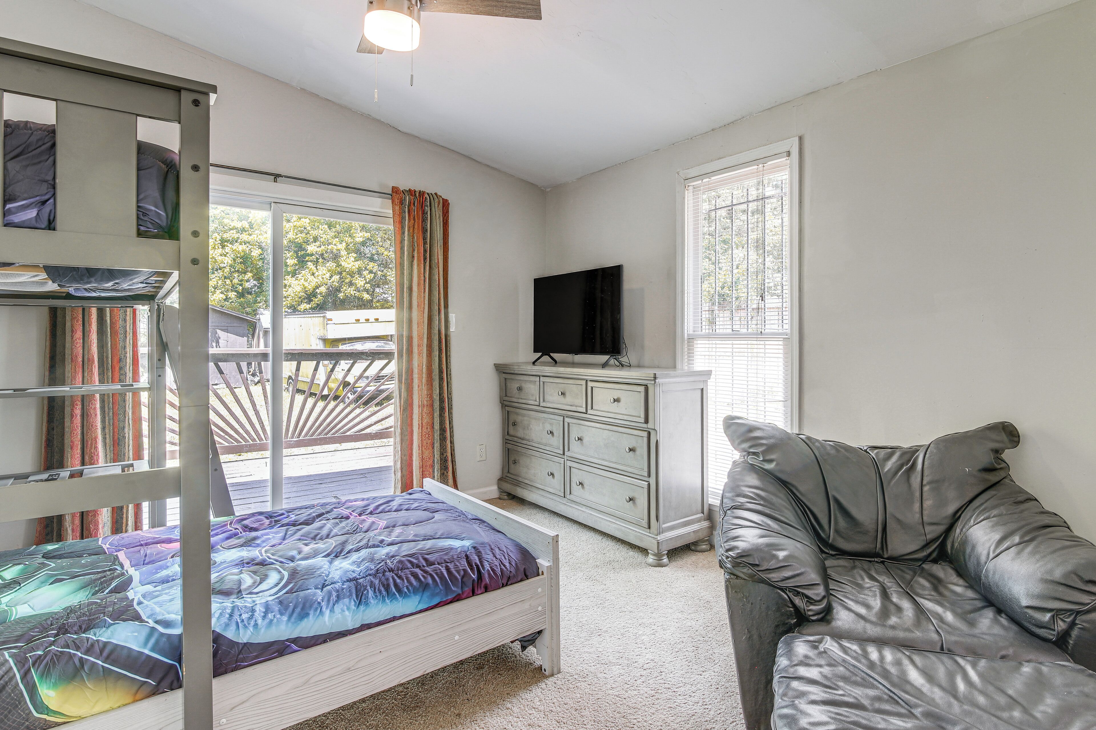 A room with a bunk bed, a dresser, a leather couch, a television, and a window with blinds.