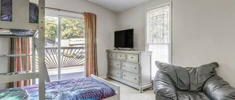 A room with a bunk bed, a dresser, a leather couch, a television, and a window with blinds.