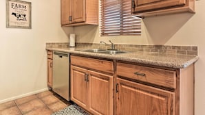 A kitchen with wooden cabinets, a granite countertop, a dishwasher, and a window with blinds. - Fenced Yards! Quiet 2-unit Combo in Tucson (Tucson)