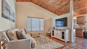A spacious living area with a high ceiling, wooden beams, a sofa, a coffee table, a TV, and a kitchen area with cabinets and a countertop. - Fenced Yards! Quiet 2-unit Combo in Tucson (Tucson)