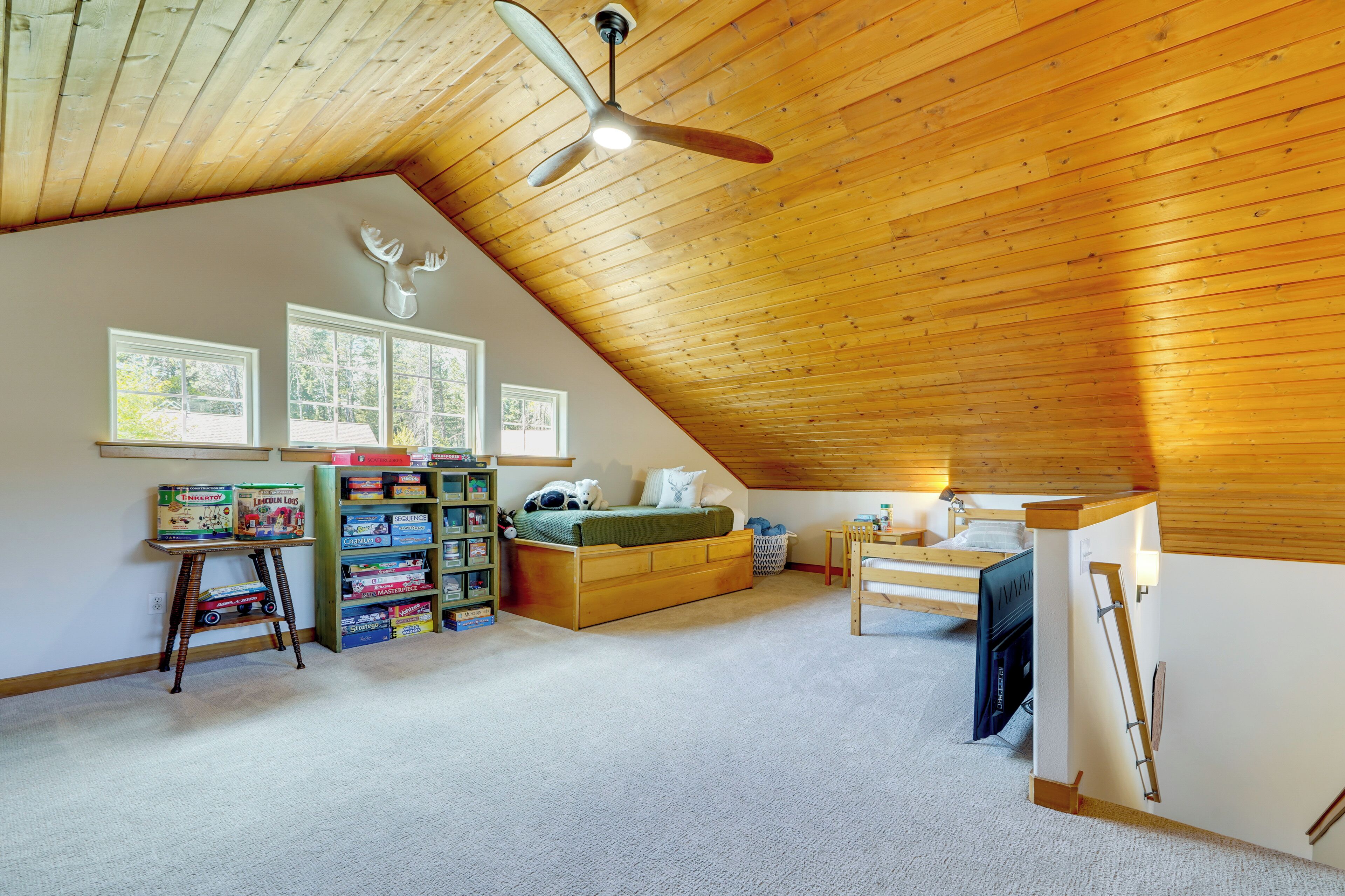 Una habitación con techo inclinado, cama, estantería y ventana.
