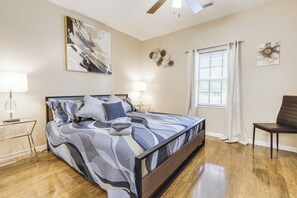 Une chambre à coucher comprenant un lit, des tables de chevet, une chaise, une fenêtre avec des rideaux et des œuvres d’art murales.