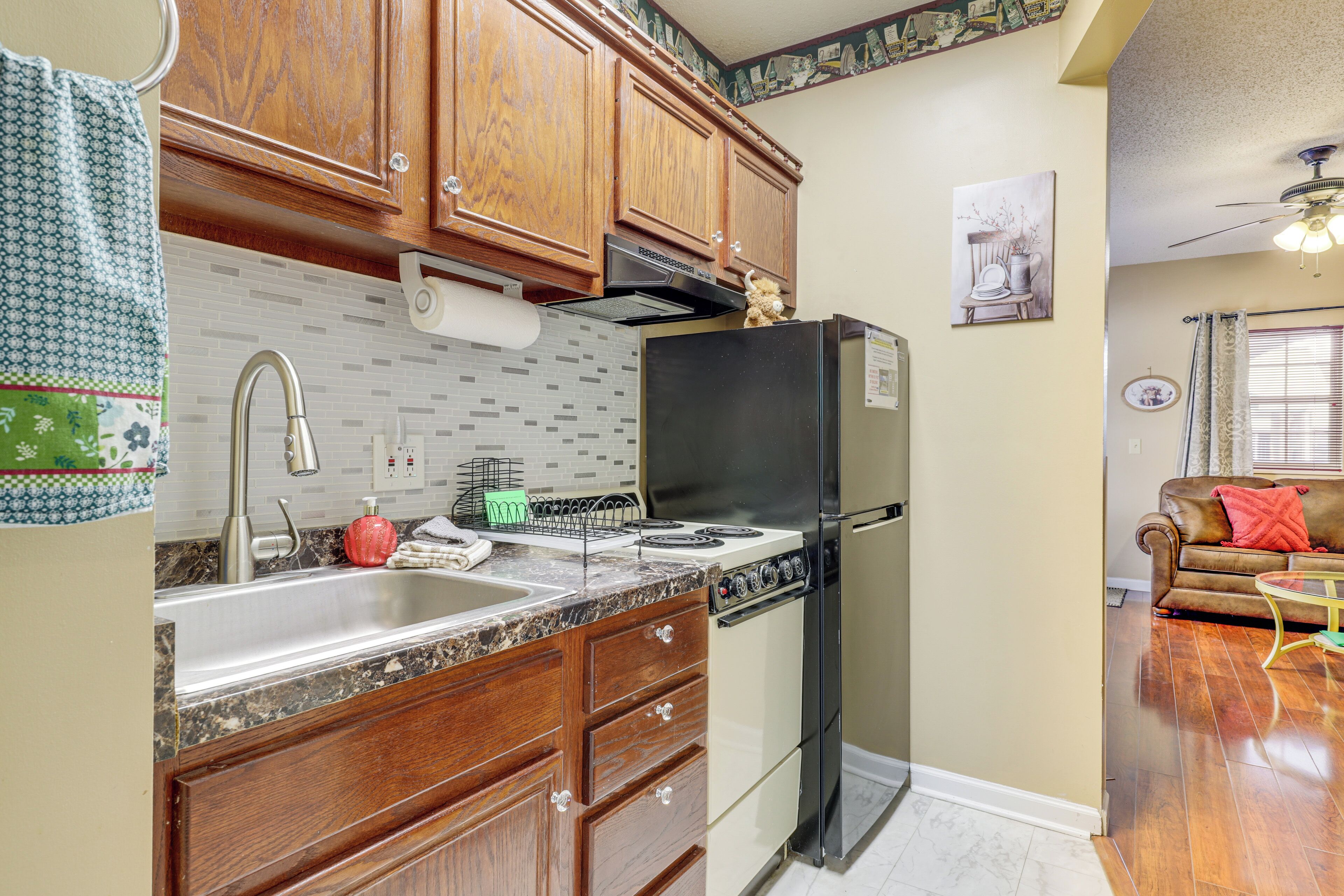 A kitchen with wooden cabinets, a stainless steel sink, a black refrigerator, and a stove.