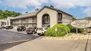 A building with a sign for 'Legacy Condominiums,' a parking lot with several cars, and a clear sky. - Walkable Retreat Near The Island! Gateway to Gsmnp (Pigeon Forge)