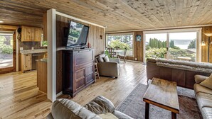 A spacious living area with a wooden ceiling, a television, a sofa, and a view of the outdoors. - Walk to Private Beach: Bay-view Whidbey Island Gem (Oak Harbor)
