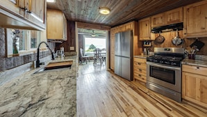 A kitchen with wooden cabinets, a stainless steel refrigerator, a stove, and a dining area with a table and chairs. - Walk to Private Beach: Bay-view Whidbey Island Gem (Oak Harbor)