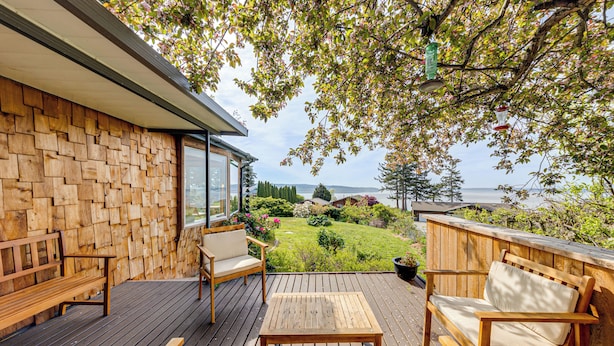 A wooden deck with outdoor furniture, a view of a garden, and a body of water in the background. - Walk to Private Beach: Bay-view Whidbey Island Gem (Oak Harbor)
