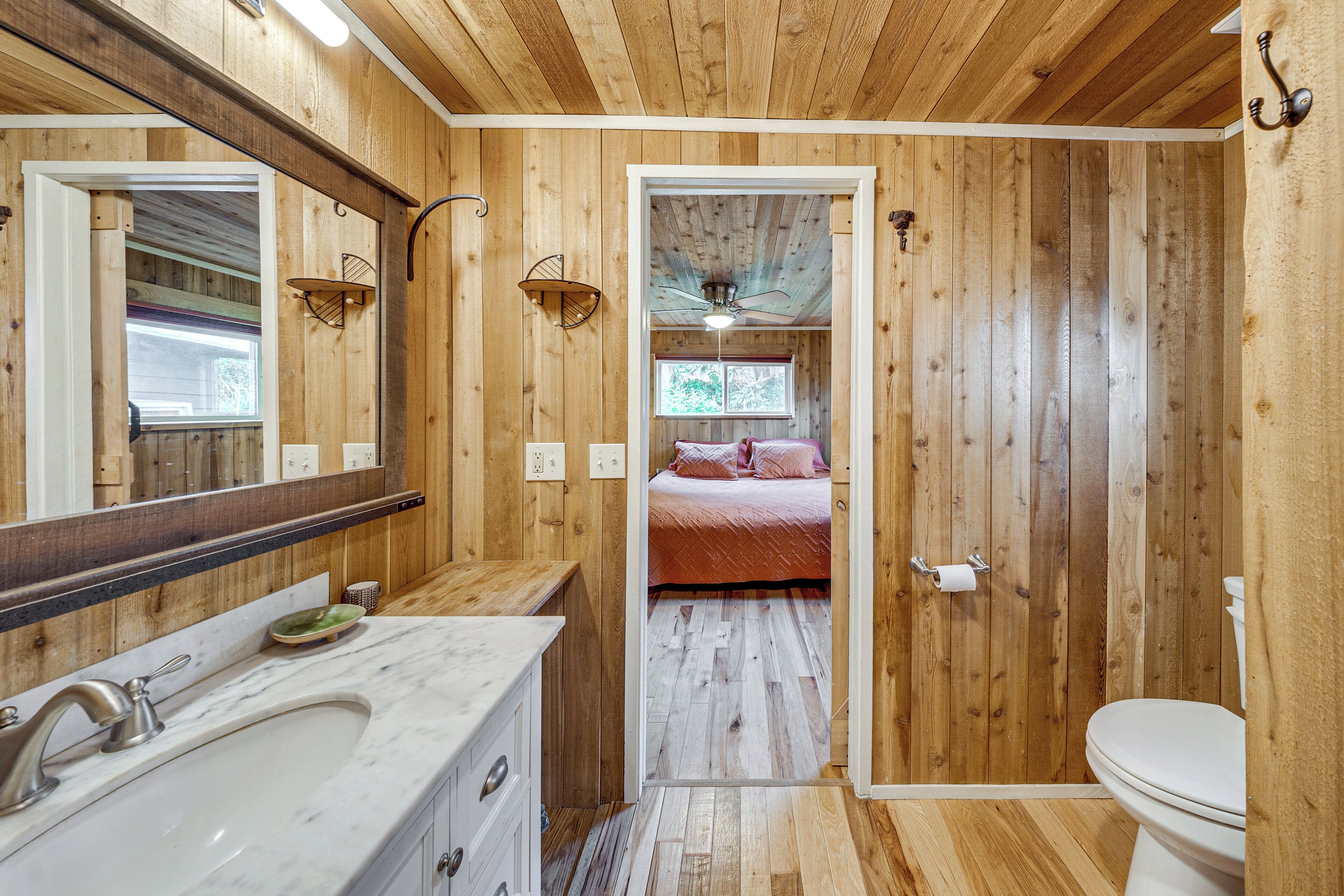 A wooden interior bathroom with a sink, mirror, and toilet.