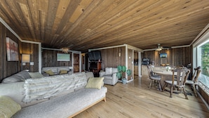 A spacious living area with a wooden ceiling, a sofa, a dining table with chairs, and a television. - Walk to Private Beach: Bay-view Whidbey Island Gem (Oak Harbor)