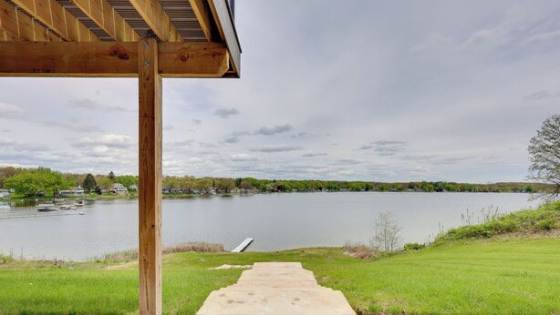Une pergola en bois surplombe un lac, et un chemin en béton mène jusqu’à la rive.