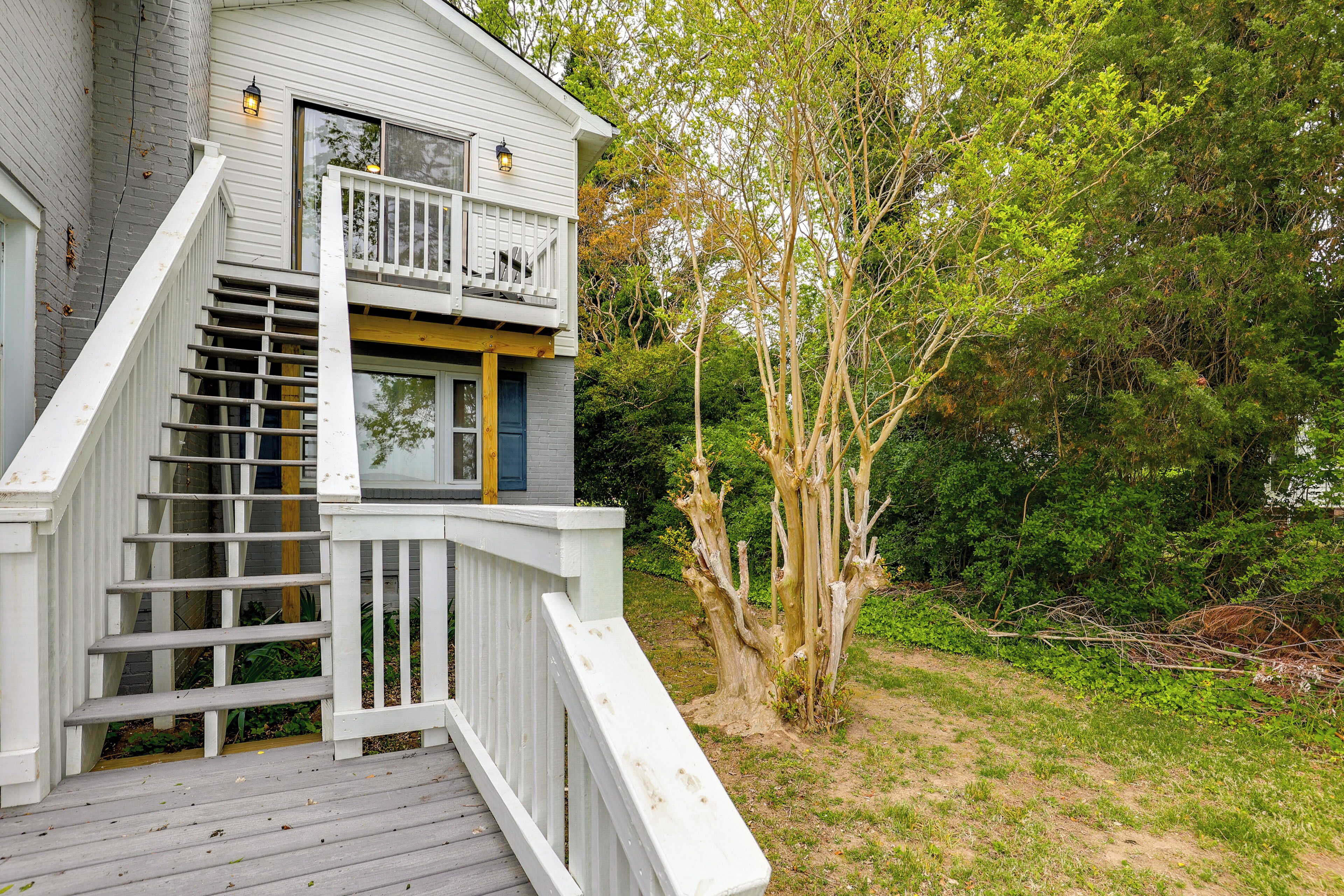 Une maison à deux étages dotée d’une terrasse en bois et d’un escalier menant à un balcon.