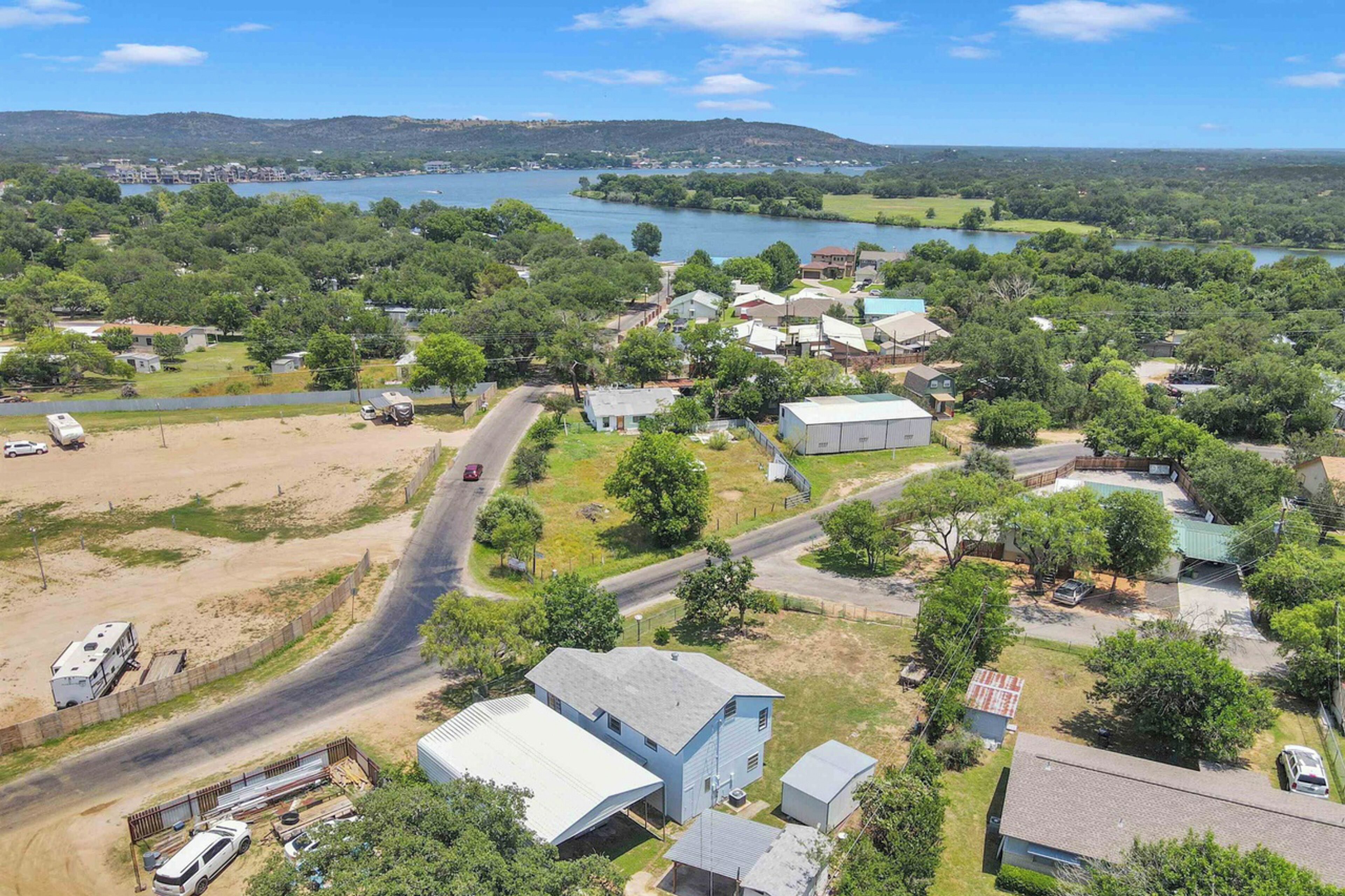 An aerial view of a residential area with houses, a road, and a body of water in the background.