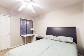 A bedroom with a bed, a desk, a chair, a ceiling fan, a window with blinds, and a door. - 2BR Condo in Fountain Hills w/ Mountain Views (Fountain Hills)