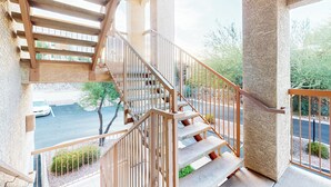 Un escalier avec une rampe métallique menant à un balcon qui donne sur un parking et sur un espace verdoyant.