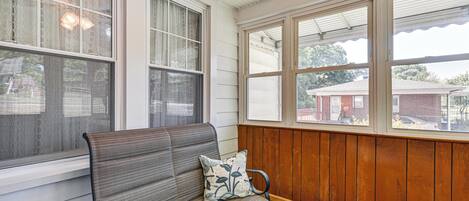 A bench with a cushion, a small table with a plant, and a view of a brick building through large windows.
