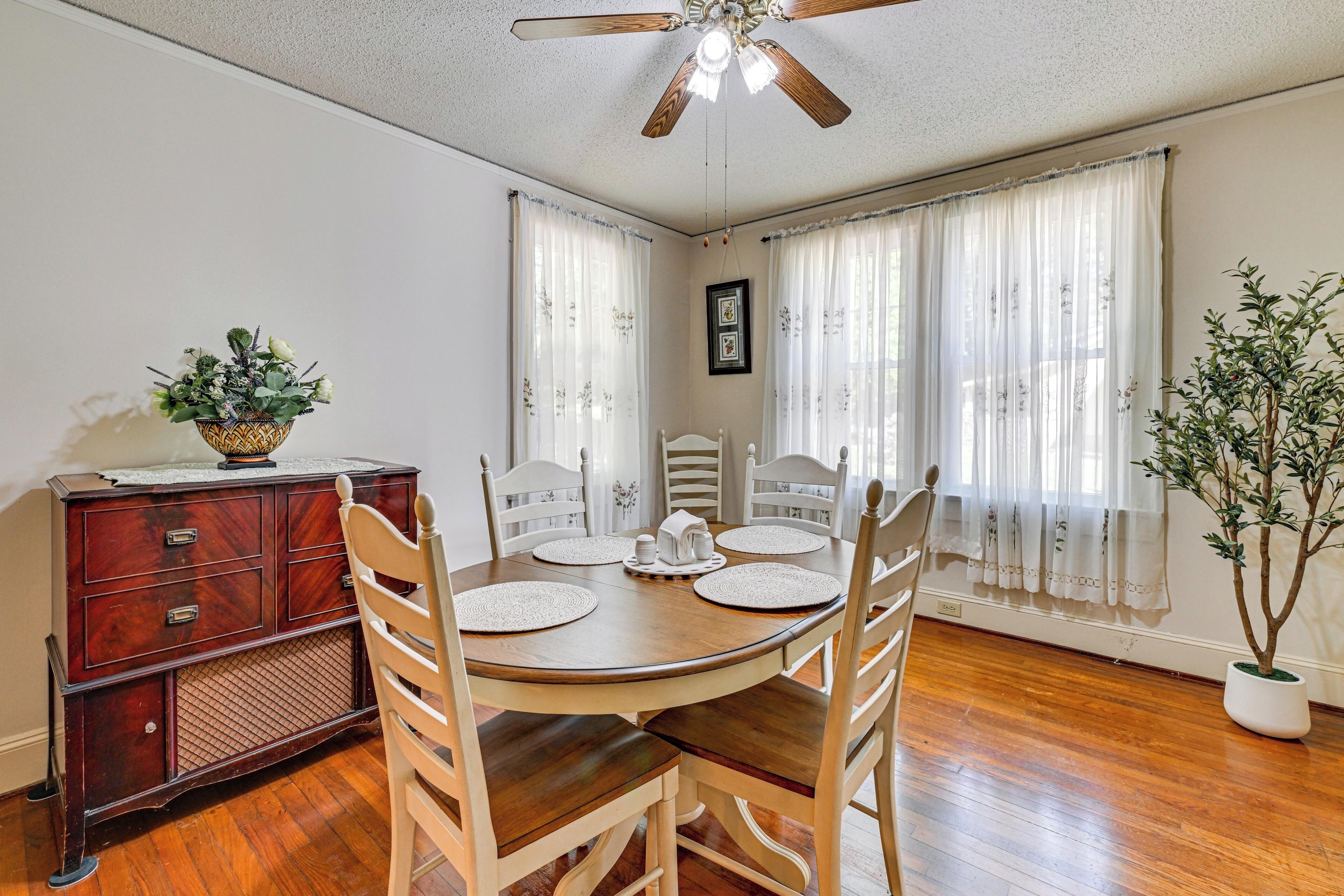 A dining area with a wooden table, white chairs, a ceiling fan, and a potted plant.