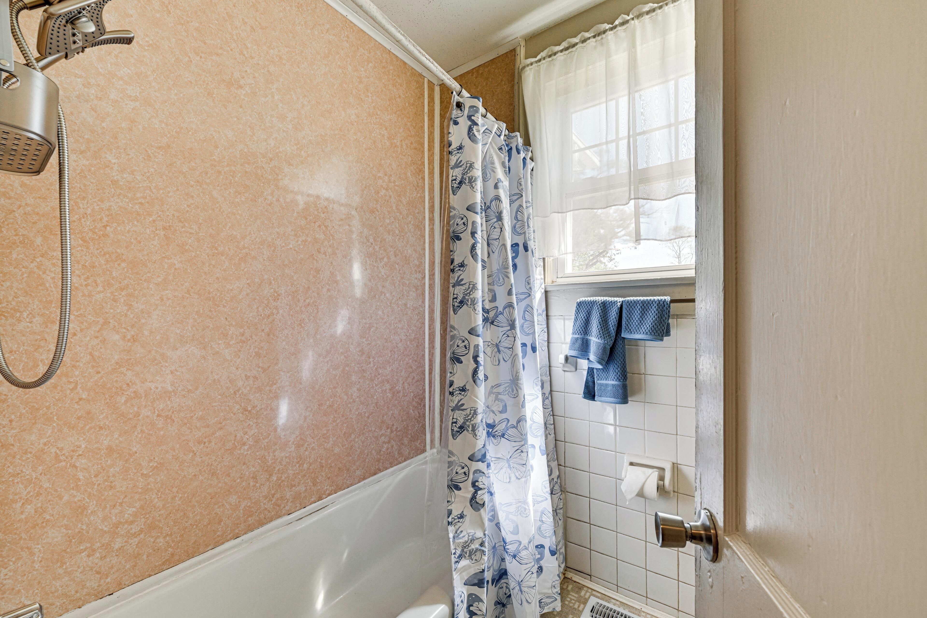 Un baño con ducha, inodoro, toallero con toallas y ventana con cortina.