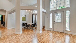 A spacious room with a high ceiling, a dining area with a table and chairs, and large windows with a view.