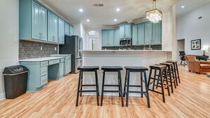 A modern kitchen with teal cabinets, a central island, bar stools, and a chandelier.
