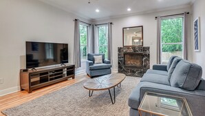 A living room with a television, sofa, armchair, fireplace, and large windows.