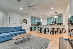 Una sala de estar moderna con un sofá, una mesa de centro y una cocina con armarios color turquesa y una barra con taburetes.
