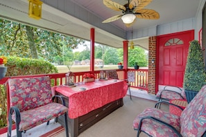 A covered porch with a table set for dining, surrounded by chairs, and a red door. - Peaceful Porch, Yard! Riverdale Home Near Dtwn ATL (Riverdale)