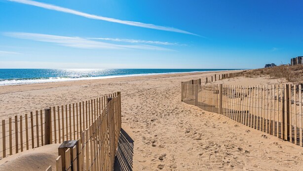 A sandy beach with wooden fences, a clear blue sky, and the ocean in the background. - 200 Feet to the Beach! Cute Ocean City Condo (Ocean City)
