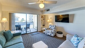 A hotel room with a ceiling fan, a sofa, a chair, a TV, a balcony with a view, and a bookshelf. - 200 Feet to the Beach! Cute Ocean City Condo (Ocean City)